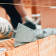 hands laying large bricks with mortar and trowel