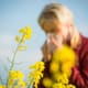 A woman sneezing next to yellow flowers.