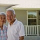 An elderly couple standing outside a house.