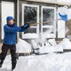 A man shoveling snow outside a house. 