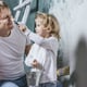 A young girl touches her dad's nose with a paintbrush.