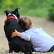 Child leaning on a black dog with a red collar