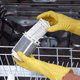 Someone wearing yellow rubber gloves removing and cleaning a dishwasher filter.