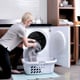 A woman on her knees putting laundry in a washing machine.