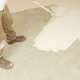 A professional painter uses a roller to spread white paint over a concrete floor.