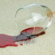 A wine glass knocked over on a carpet with spilled red wine.