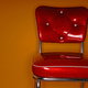 A red vinyl chair against an orange wall.