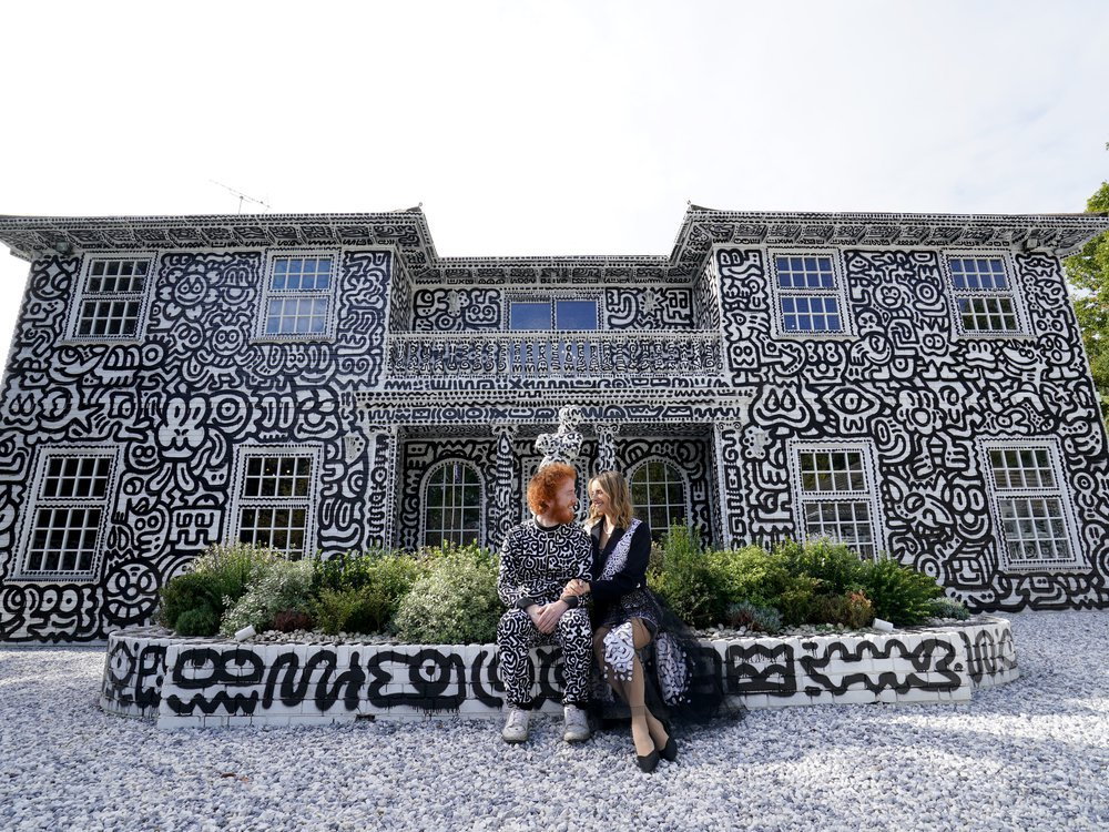 Sam and Alena Cox (aka Mr. and Mrs. Doodle) look lovingly at each other in front of their doodle-covered mansion in Kent, England. 