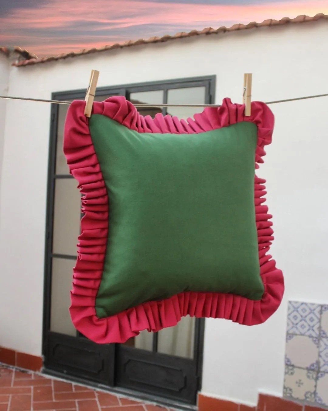 Red and green throw pillow by Paboy Bojang hangs on a clothes line.