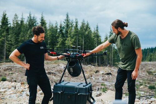 Two men prepare a Flash Forest seed-shooting drone for take off in a forest area. 