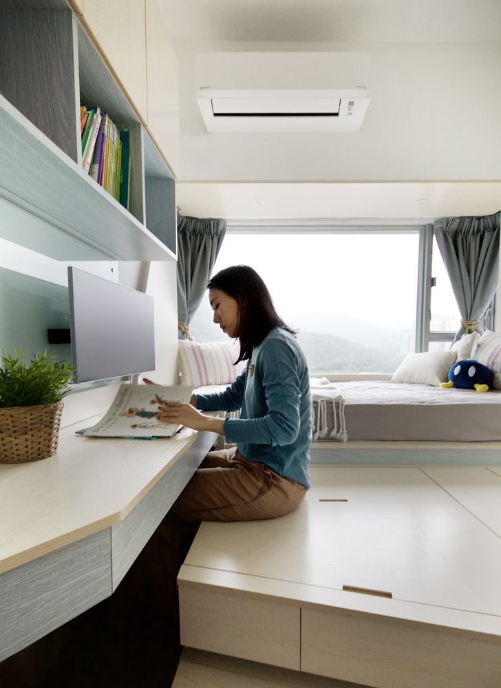 Woman reads a magazine/works at a built-in desk in the Smart Zendo apartment's master bedroom area, with the storage unit under her doubling as seating.