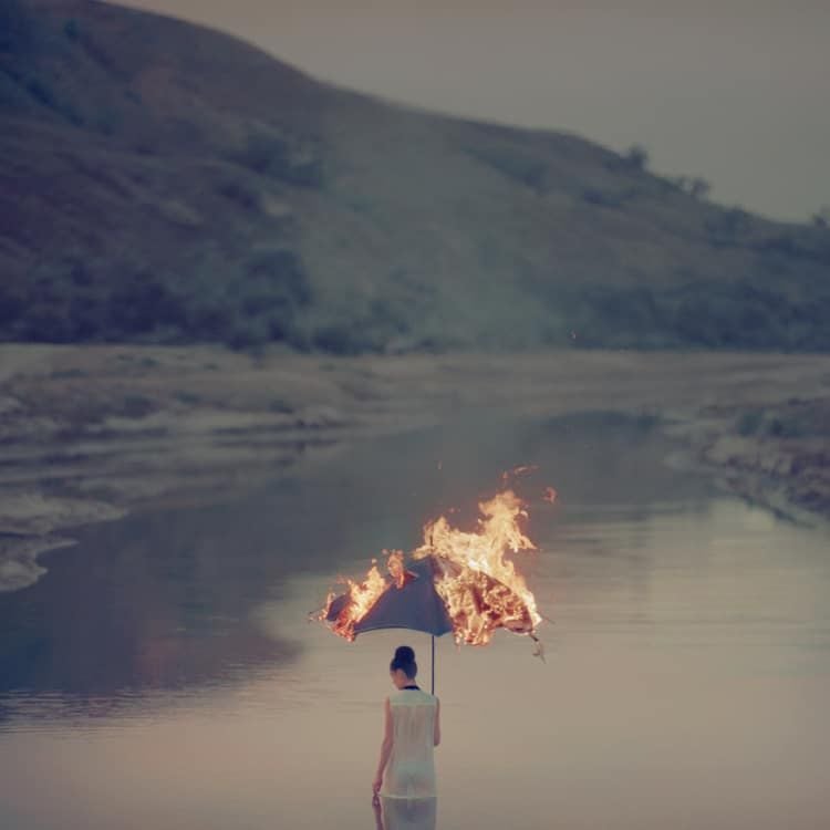 Surreal photograph by Ukrainian artist Oleg Oprisco shows a woman walking into a lake with a burning umbrella.