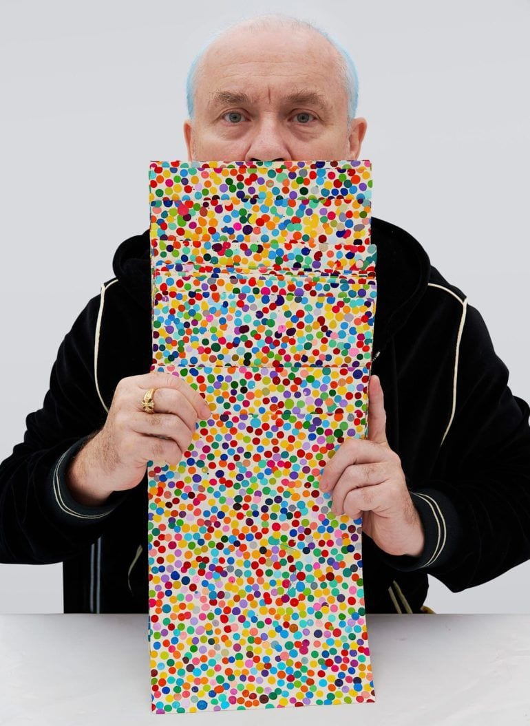 Damien Hirst holds up physical versions of the 
