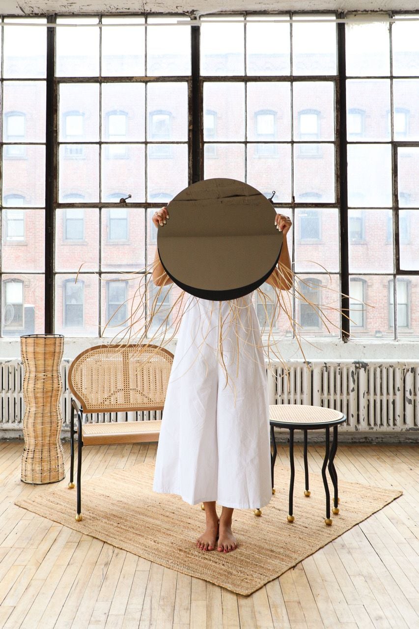 Woman holds up the sculptural Lolo mirror featured in Cheyenne Concepcion's RECLAIM furniture collection.