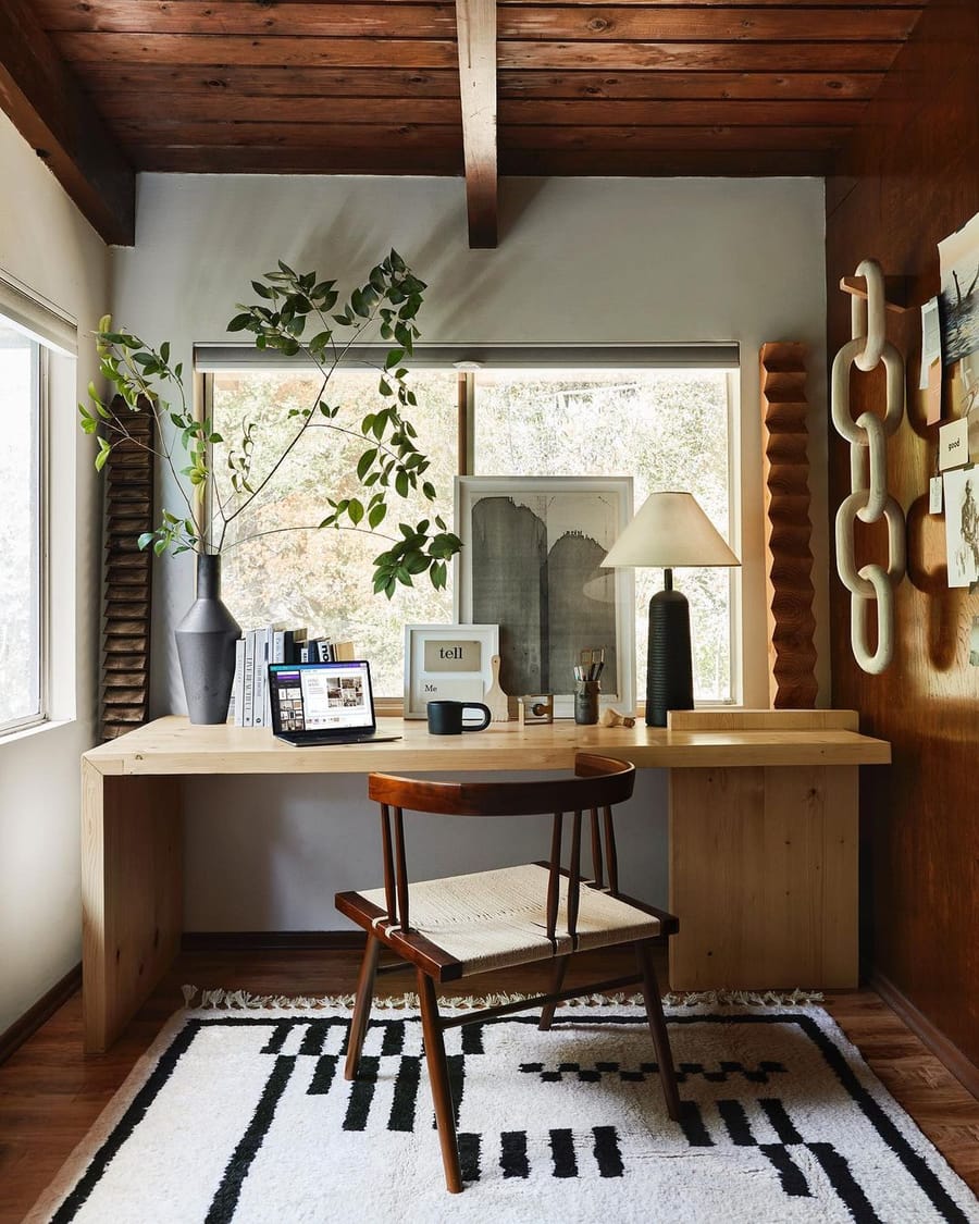Rich wooden office space is brought to life with hanging greenery, sculptural decor, and a striking floor rug. 