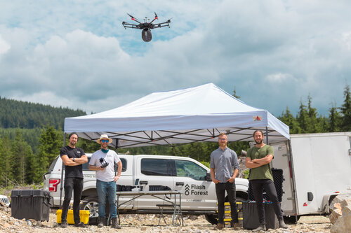 Flash Forest employees smile proudly beneath one of their AI-powered, seed shooting drones.