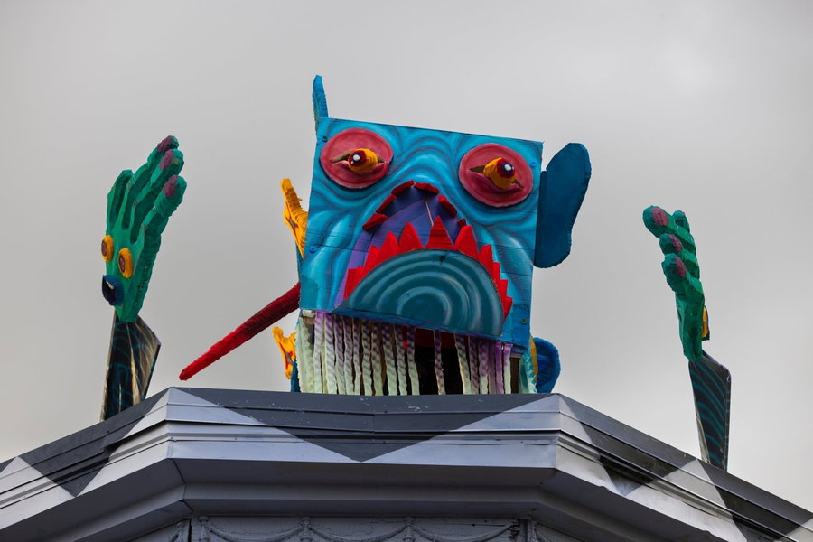 Head of another monstrous puppet pops out of the building's roof.