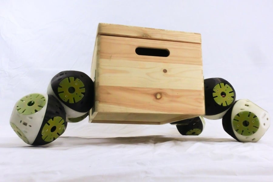 A group of Roombots work together to move a wooden box. 