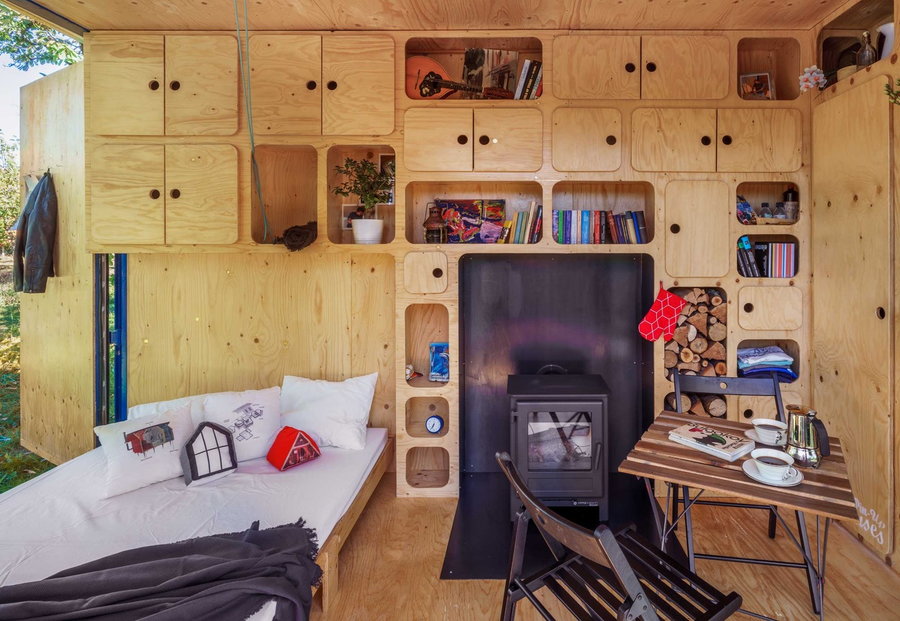 Inside the Gaia Off-Grid Container House a fold-out bed offers a small sleeping space alongside a cozy wood-burning stove.