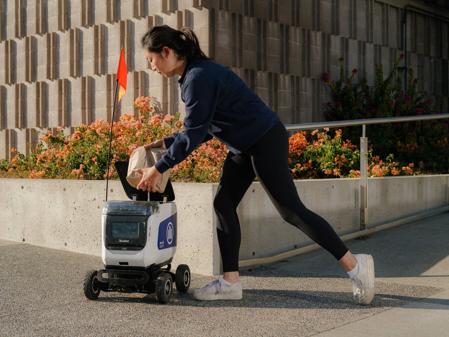 Young woman loads a package into the iF Design Award-winning Kiwibot Plus.
