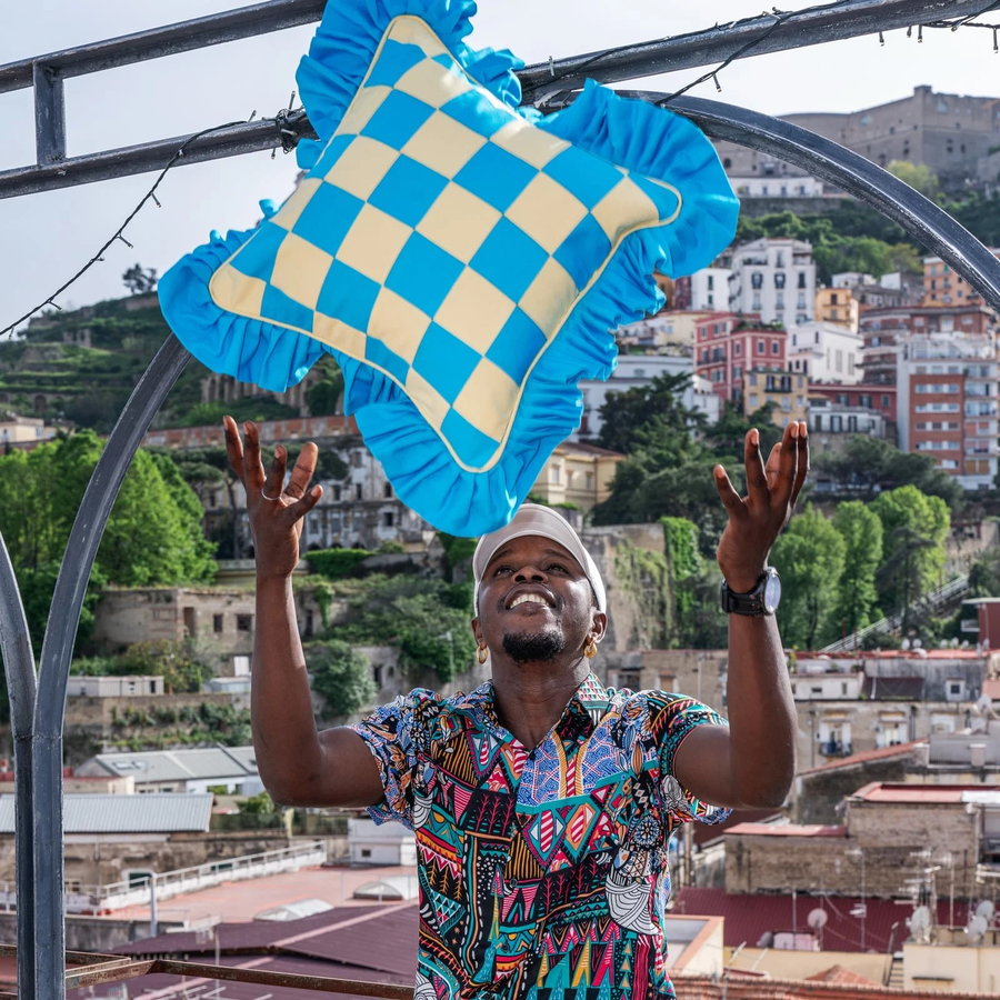 Artisan Paboy Bojang happily throws one of his colorful handmade throw pillows up in the air.