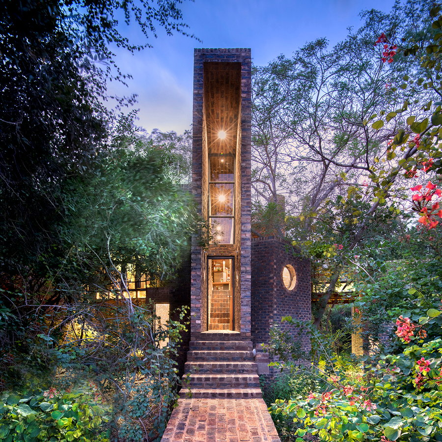 The narrow House of the Big Arch emits a warm glow as the sun sets over the surrounding South African forest.