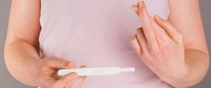 A woman crossing her fingers while holding a pregnancy test.
