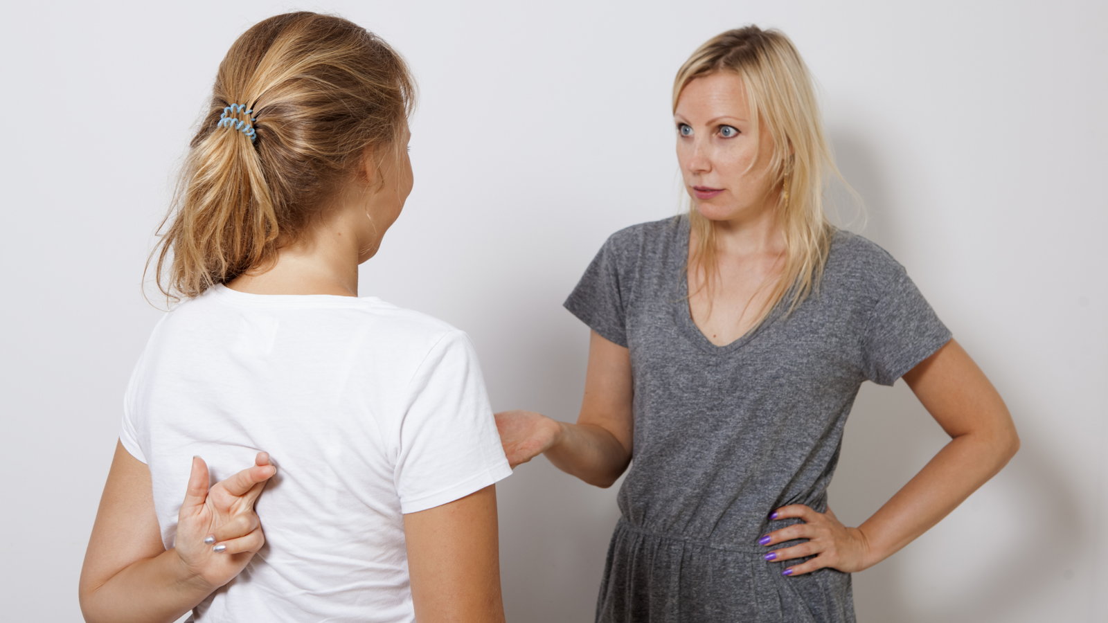 mom talking to teen who has fingers crossed behind her back