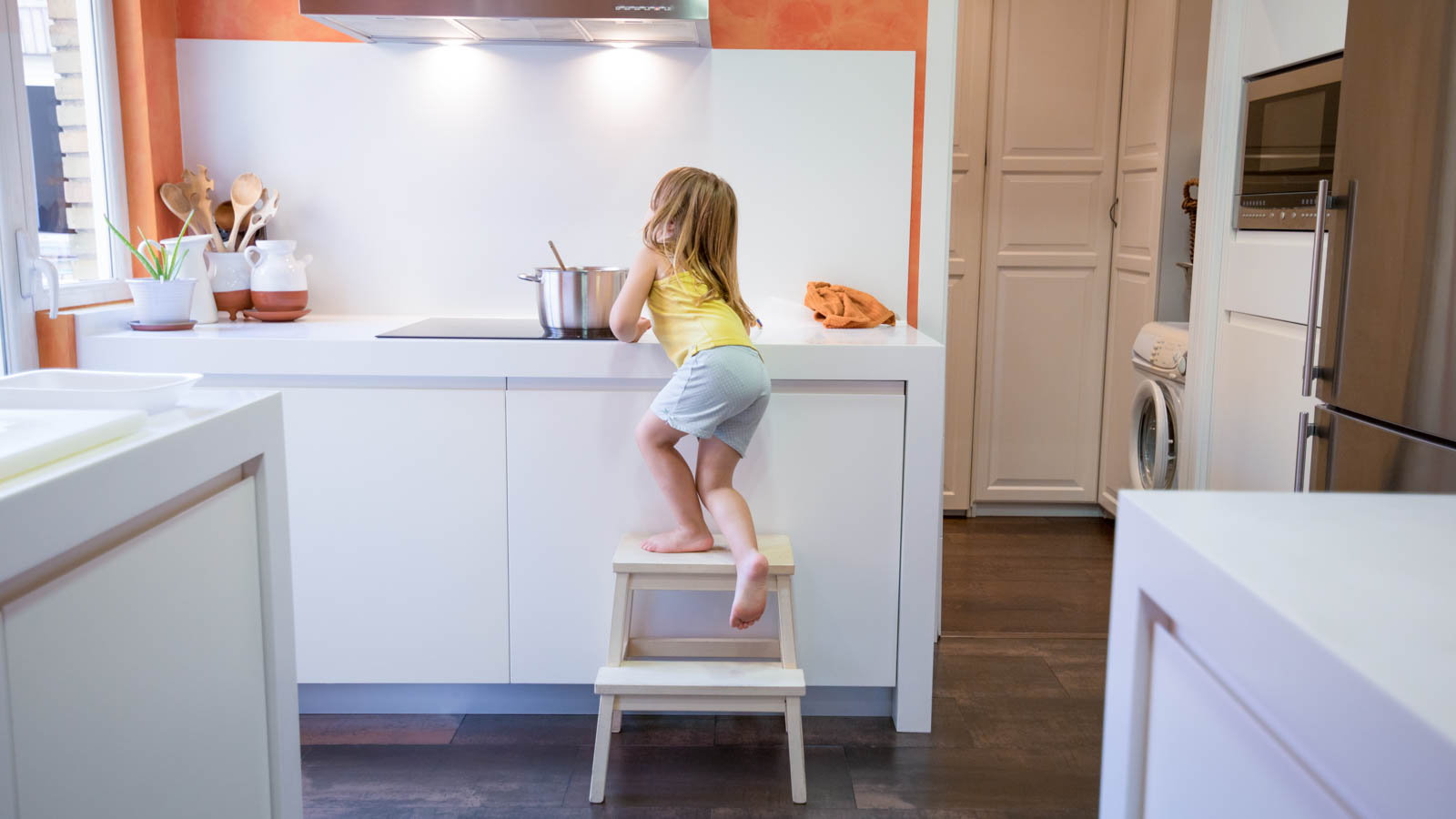 child stepping on stool to reach stove top