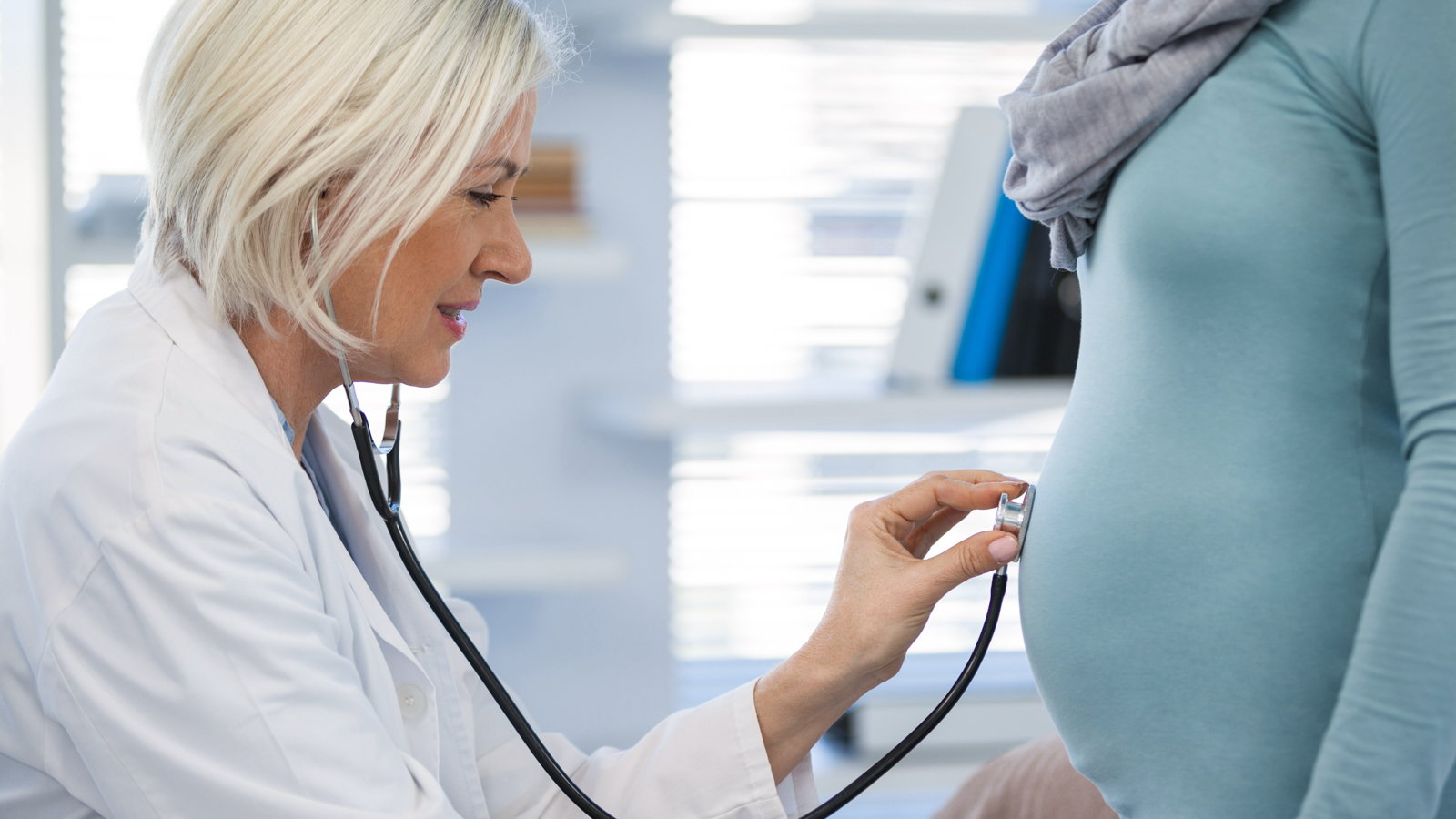 doctor listening to pregnant woman's stomach with stethoscope