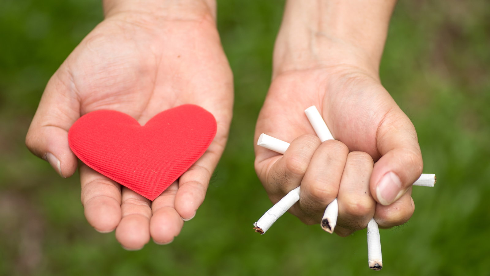 woman holding paper heart in one hand and crushed cigarettes in the other