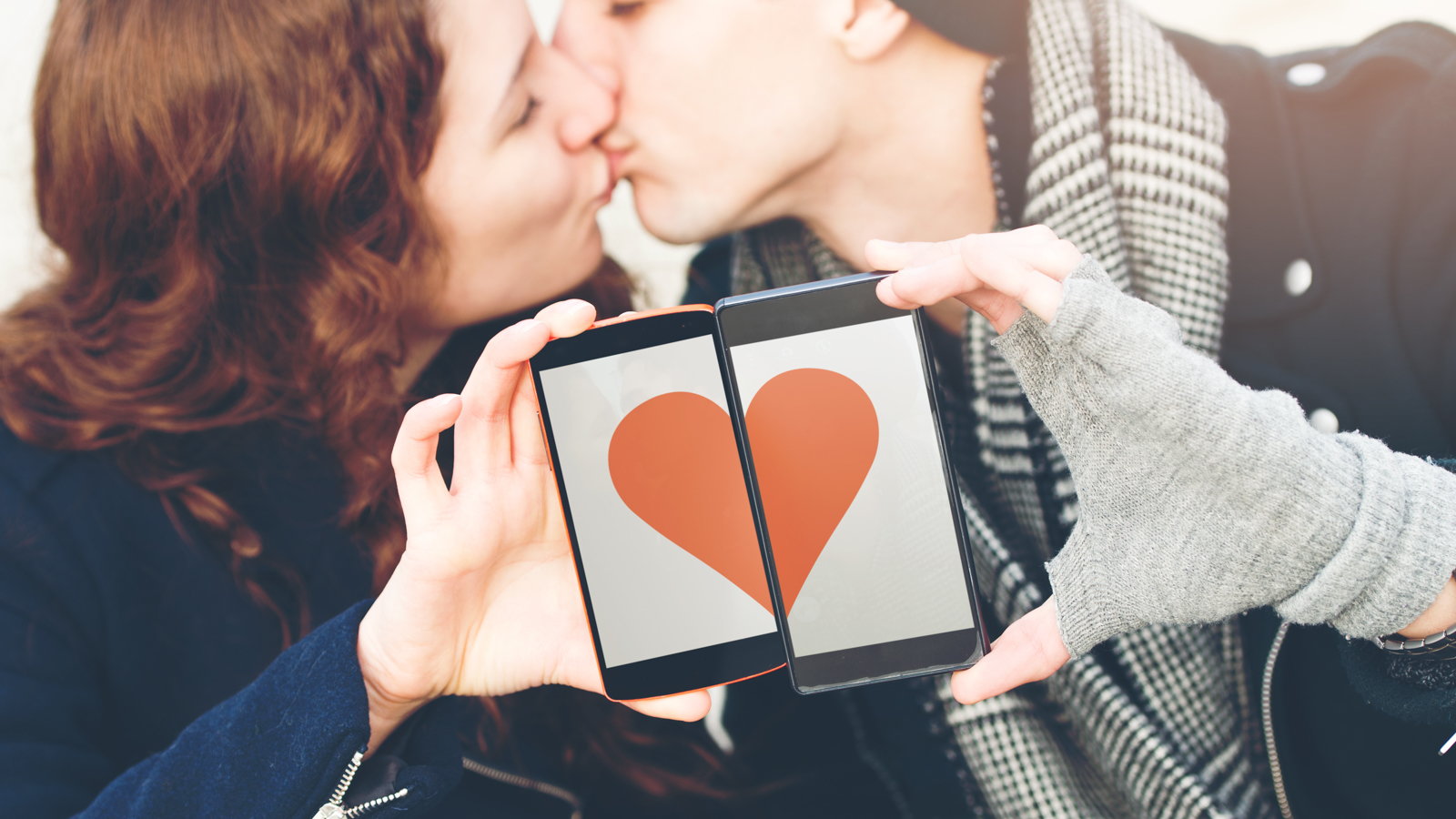 teen couple kissing and holding cell phones