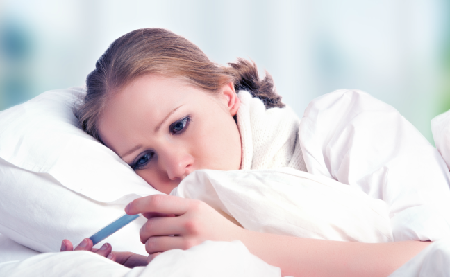 A woman in bed reading her temperature on a thermometer. 