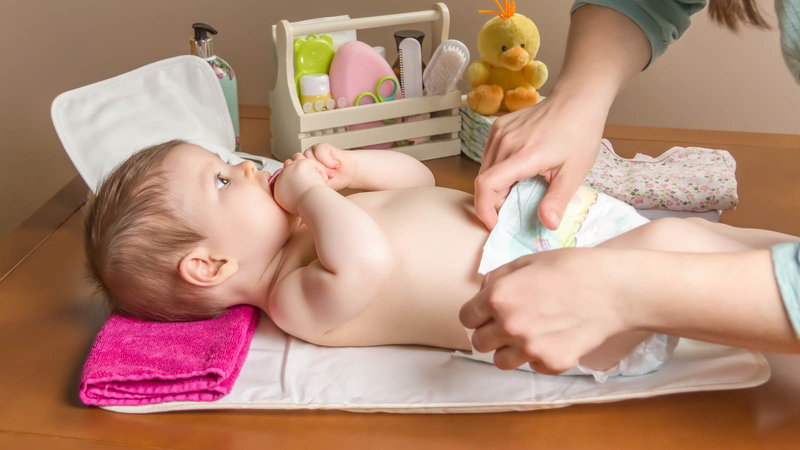 Mother changing baby on table with hygiene suplies