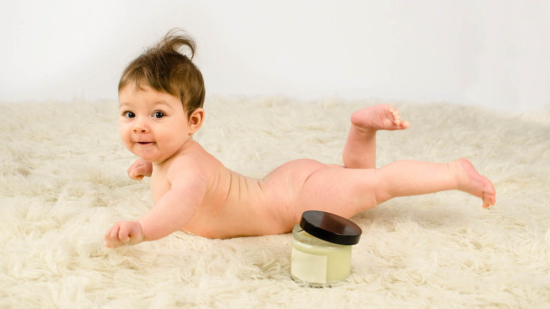 Naked baby on rug with cream