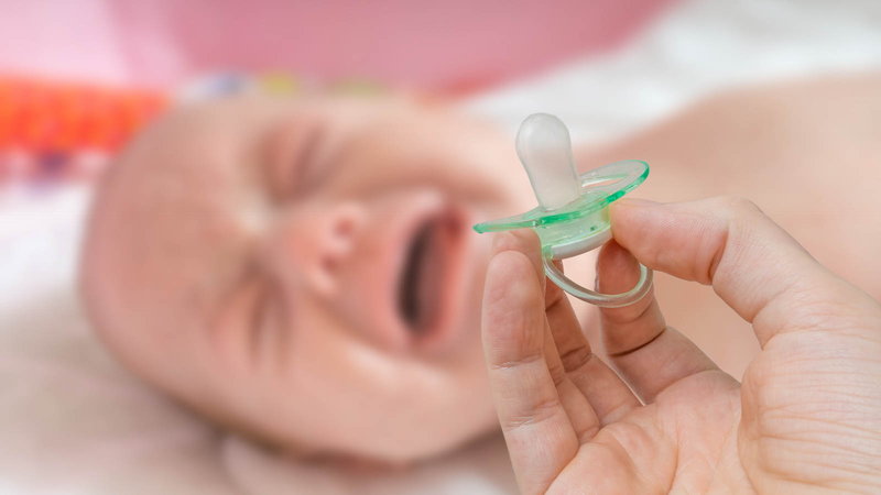 mom holding pacifier next to crying baby