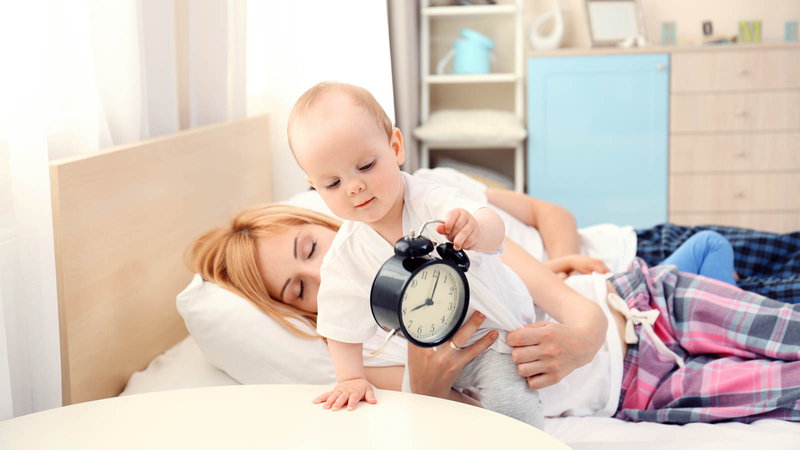 Baby holding a clock with mother on bed