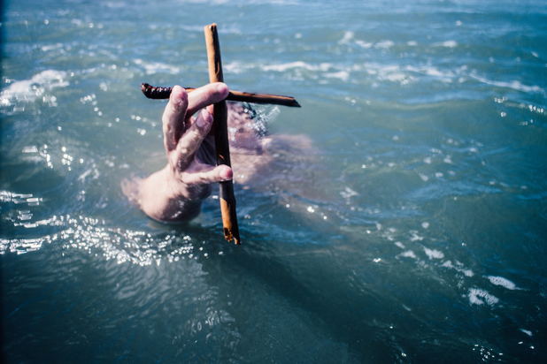 hand holding onto cross in the water
