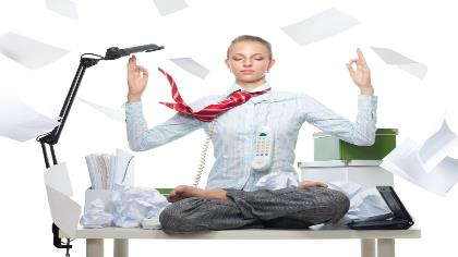 A woman sits on her desk meditating as she is surrounded by office work. 
