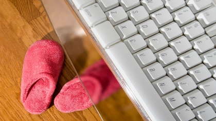 A pair of pink slippers underneath a desk with a computer keyboard on it. 