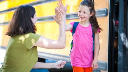 A mom giving her daughter a high-five near a school bus.