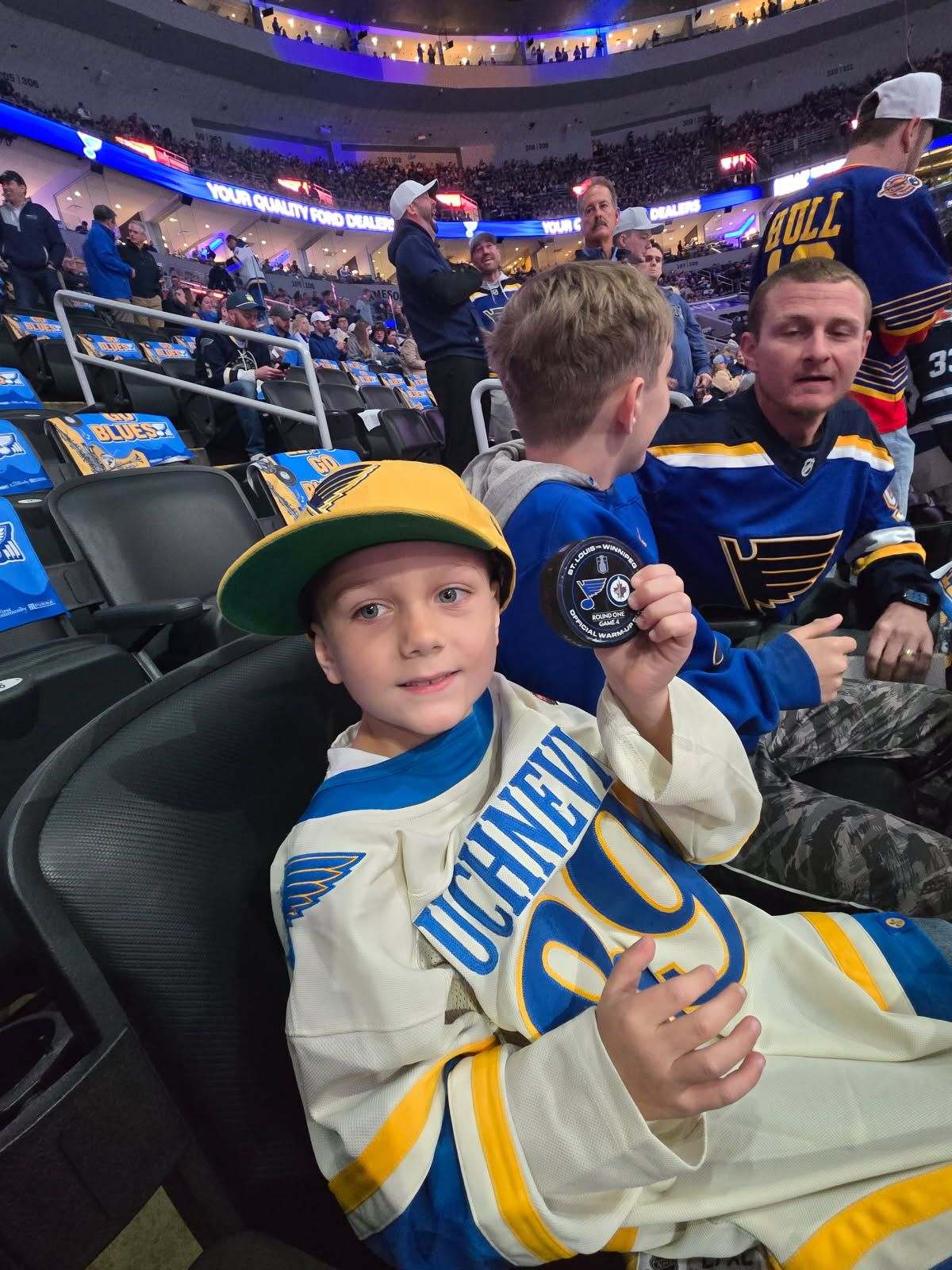 In order down the row, Grandson Keegan, Gabe, and SIL Justin.  They're sitting in the 2nd row behind the Blues' bench right now in the 4th game of the Blues' NHL Playoff Series against the Winnepeg Jets . Keegan caught a puck that got flipped into the stands.  Game is 1-1 after the 1st Period.