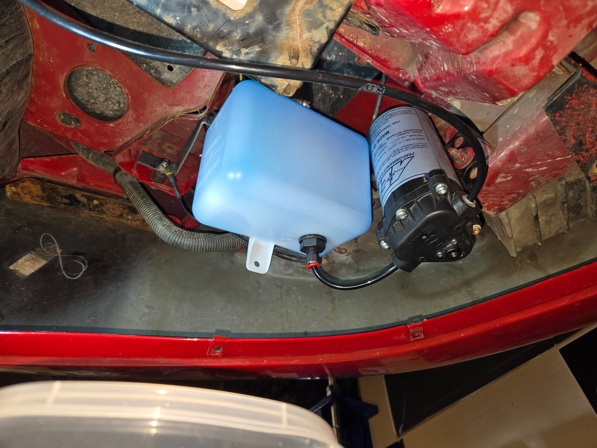 Tank and pump mounted near turn signal underneath car.