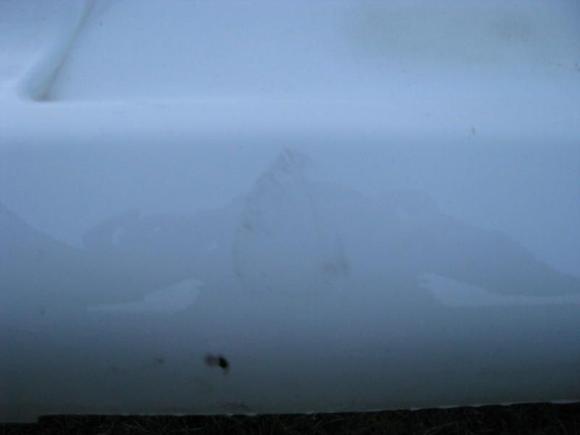 I believe this is from a garbage can that blew into the bumper on a windy day.  Wax might take this off.  This is right below where the license plate mounts.