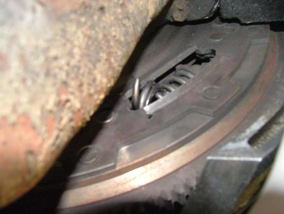 Broken DMF spring sticking out of the front of the flywheel.  The piece is twisted into the rest of spring.  At the top of the spring is the plastic piece that holds the spring in place.  The piece for the bottom broke up, part is still in the middle of the spring just above the broken piece.